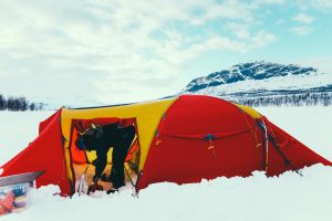 woman preparing red and yellow expedition tent in arctic on weeklong dog sledding expedition