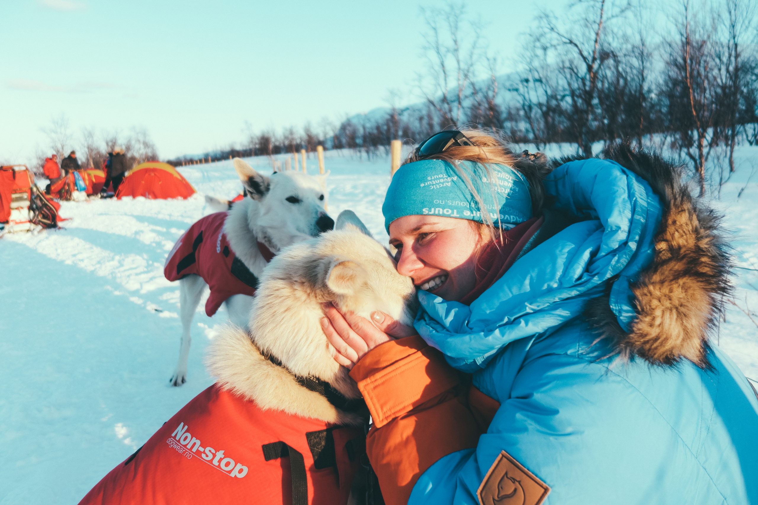 woman in blue polar parka cuddling husky in red non stop coat