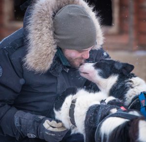 black and white husky kissing mushers dog handler face
